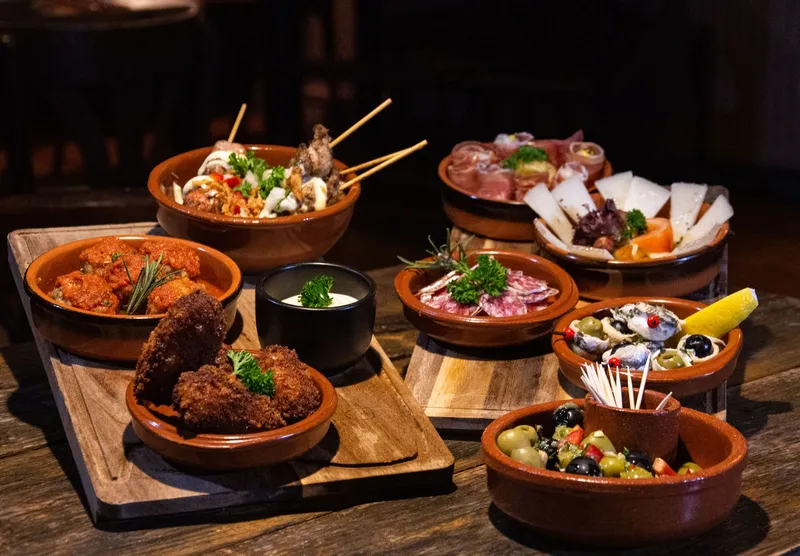 Cazuelas de barro con tapas españolas variadas sobre una mesa de madera