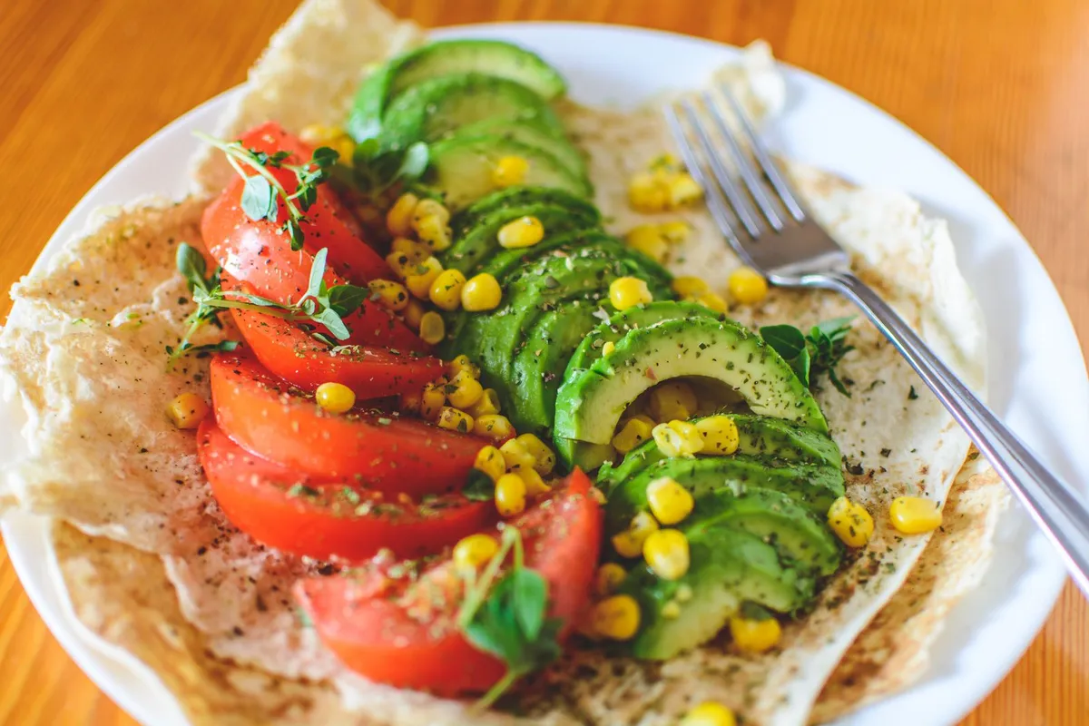 Persona pensando frente a una mesa con verdura fresca, fruta y pescado, dudando sobre si la dieta antiinflamatoria existe